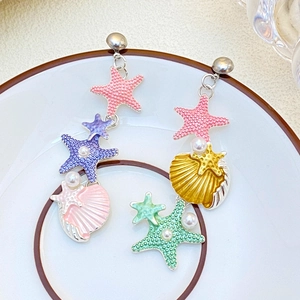 Dettaglio di orecchini oceanici asimmetrici con stelle, conchiglie, smalto e perle