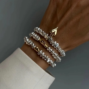 Détail de bracelets en perles CCB argentées avec pendentif coeur doré porté au poignet