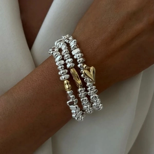 Détail de trois bracelets en perles irrégulières avec un pendentif cœur doré au poignet