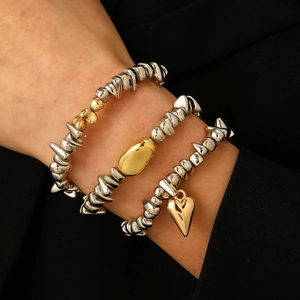 Gros plan de bracelets superposés argentés et dorés avec pendentif cœur au poignet