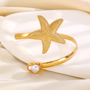 Detailed macro view of golden starfish arm cuff with a baroque pearl on fabric