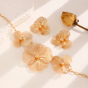 Detailed view of luxury gold hollow flower necklace and earring set on a textured stone