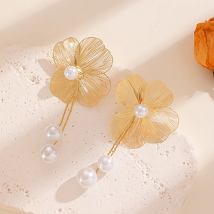 Detailed macro view of golden metal flower earrings with pearls on white stone surface