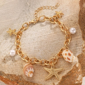 Golden ocean charm bracelet with starfish, pearl and seashell on a beach stone backdrop