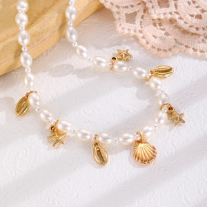 Macro detail of summer beach necklace featuring white pearls and gold starfish shell charms