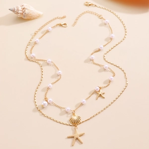 Macro view of gold shell and starfish charms with pearls on layered seaside necklace