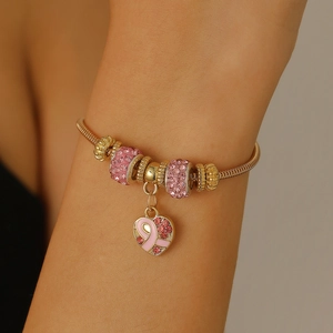 Gros plan d'un bracelet doré avec pendentif cœur ruban rose et perles en cristal