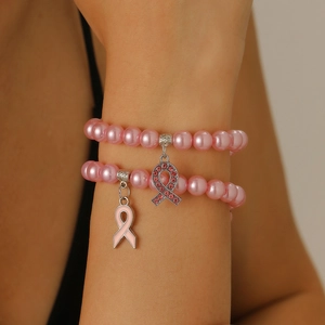 Gros plan d'un bracelet en perles roses avec un ruban rose en strass et un pendentif émaillé