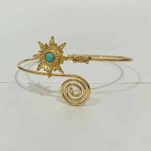 Détail d'un bracelet ouvert doré bohème avec motif spirale et disque fleur turquoise