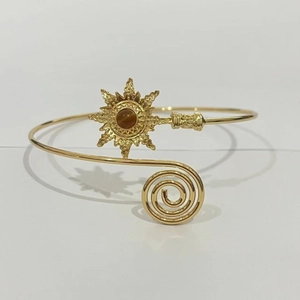 Détail d'un bracelet de bras doré avec motif soleil et pierre précieuse marron centrale