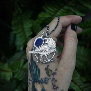 Dettaglio del ciondolo a corvo in argento vintage con gemma blu e catena rustica