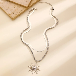 Dettaglio macro della collana a doppio strato argento con pendente a sole su fondo di pietra