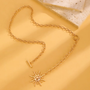 Dettaglio della collana con ciondolo a sole dorato e chiusura OT su pietra calda