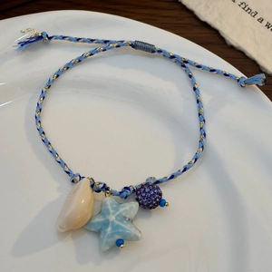 Dettaglio della collana intrecciata a tema marino con stella marina, conchiglia e ciondolo