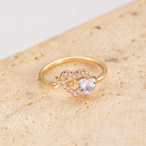 Detail of gold-plated heart ring with zircon arrow on a beige stone surface