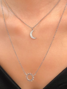 Close-up of layered silver necklace featuring delicate sun and moon pendants on a model