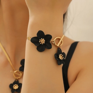 Détail d'un bracelet doré avec des breloques fleurs noires mates et un fermoir OT