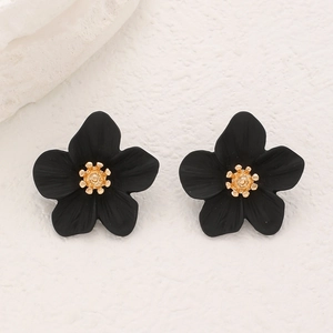 Gros plan de boucles d'oreilles fleurs noires élégantes avec centres dorés sur fond blanc