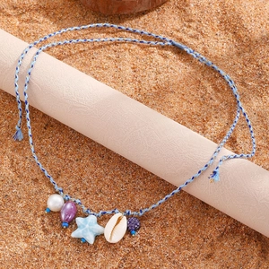 Collana boho con stella marina, ciondoli a conchiglia e perle su uno sfondo di sabbia