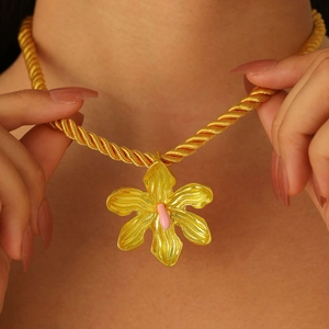 Primer plano de collar de cadena dorada con colgante de flor de esmalte rosa en modelo