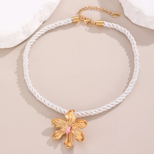 Detailed close-up of a golden flower pendant on a white braided cotton rope chain