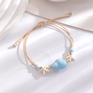 Detailed macro view of ceramic shell and starfish charms on a woven summer beach bracelet
