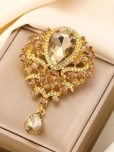 Macro detail of baroque gold alloy brooch with champagne crystal and hanging pear gem