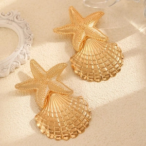 Detailed close-up of golden starfish and seashell earrings on a sandy beach background