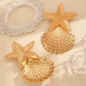 Detailed close-up of chunky gold starfish and seashell statement earrings with metallic texture