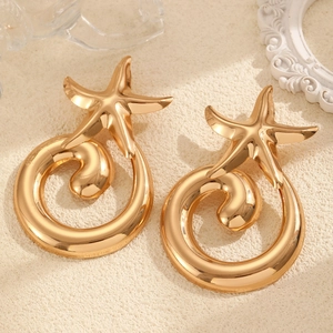 Macro view of gold starfish earrings with spiral rings on a sandy texture background