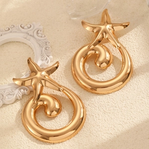 Detail of gold starfish earrings with thick spiral hoops on a sandy background