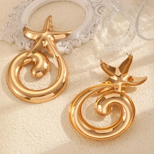 Macro detail of oversized gold starfish and spiral drop earrings with a metallic finish