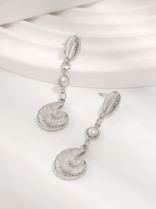 Macro detail of silver nautilus shell drop earrings with elegant white pearl accent