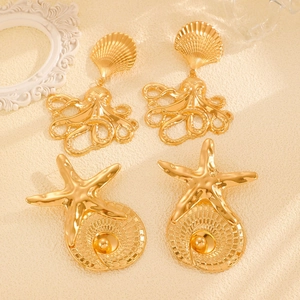 Detailed view of gold octopus and starfish stud earrings with pearls on sandy background