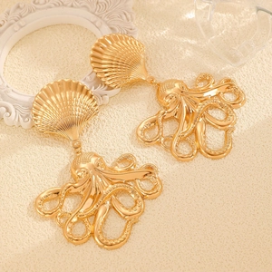 Detailed close-up of gold-plated octopus and seashell drop earrings on a beige textured base