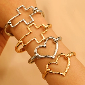 Detail showing stacked cross and heart open bangles with hammered texture in gold and silver