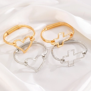 Detail of silver and gold cuff bracelets featuring hollow heart and cross charms
