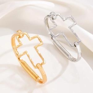 Macro shot of silver and gold open bracelets with hollow cross design on silk background