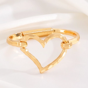 Detailed macro of golden heart bracelet featuring textured surface and spring hinge