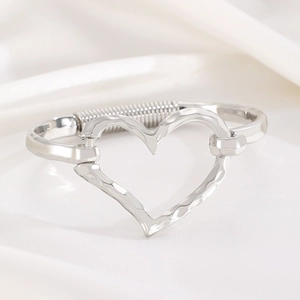 Detail of silver hammered heart bracelet with flexible screw texture band on silk fabric