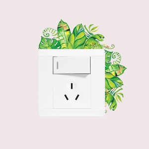 Détail d'un interrupteur mural blanc et d'une prise avec décorations de feuilles vertes