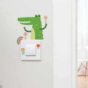 Detailed view of green crocodile and rainbow cartoon stickers on a light wall switch