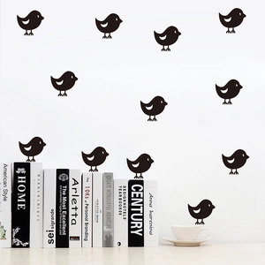 Detail of minimalist black bird wall stickers on a white wall above books and coffee cup