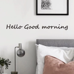 Hello Good Morning wall decal in black cursive font above a bed in a cozy bedroom