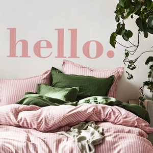 Pink and white striped bedding set with dark green pillows in a bright interior
