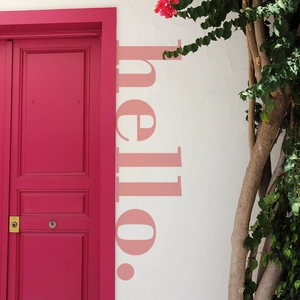 Vertical pink hello wall sticker displayed on a bright magenta wooden door with green plants