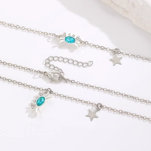 Detalle del colgante de cangrejo con gema azul y dije de estrella en cadena plateada