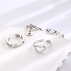 Close-up of four silver heart rings with hollow designs on a white stone pedestal