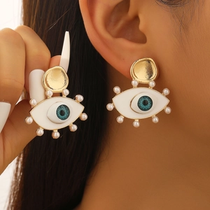 Macro detail of Evil Eye earrings with blue zircon and white pearl accents on golden base
