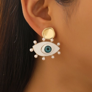 Macro view of gold Evil Eye earring with white pearls and blue enamel detailing on model